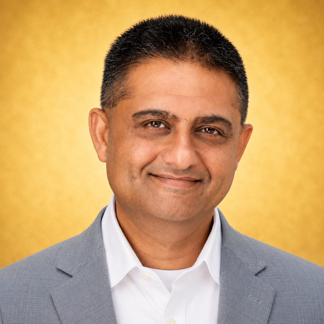 A person in a gray suit with a yellow background.